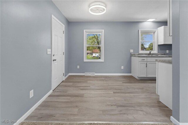 unfurnished dining area with plenty of natural light, visible vents, light wood-style flooring, and baseboards
