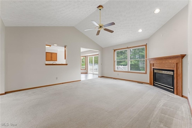 unfurnished living room featuring lofted ceiling, baseboards, a glass covered fireplace, ceiling fan, and light colored carpet