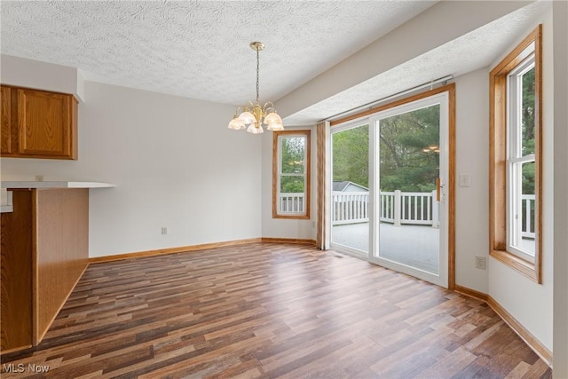 unfurnished dining area with baseboards, a notable chandelier, a textured ceiling, and wood finished floors