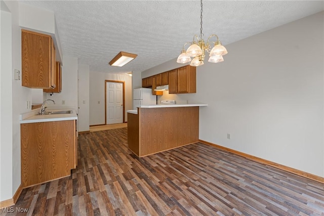 kitchen featuring a sink, a peninsula, brown cabinetry, freestanding refrigerator, and dark wood-style flooring