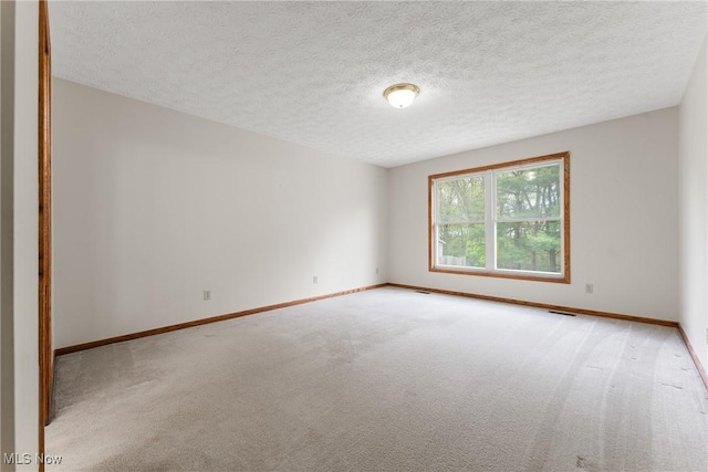 empty room with a textured ceiling, carpet flooring, baseboards, and visible vents