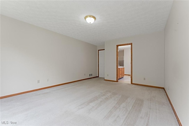 spare room featuring a textured ceiling, visible vents, baseboards, and light carpet