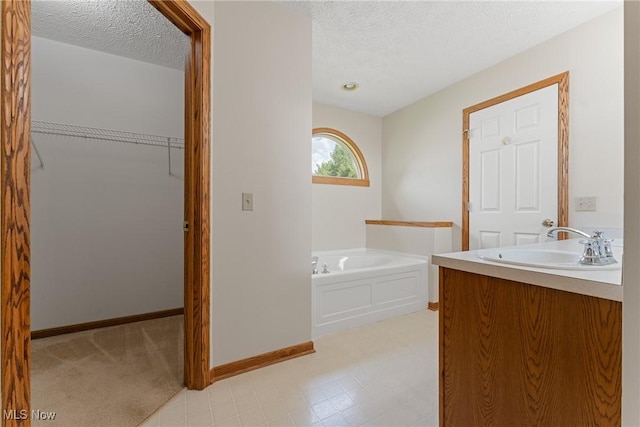 full bathroom with vanity, a textured ceiling, a spacious closet, baseboards, and a bath
