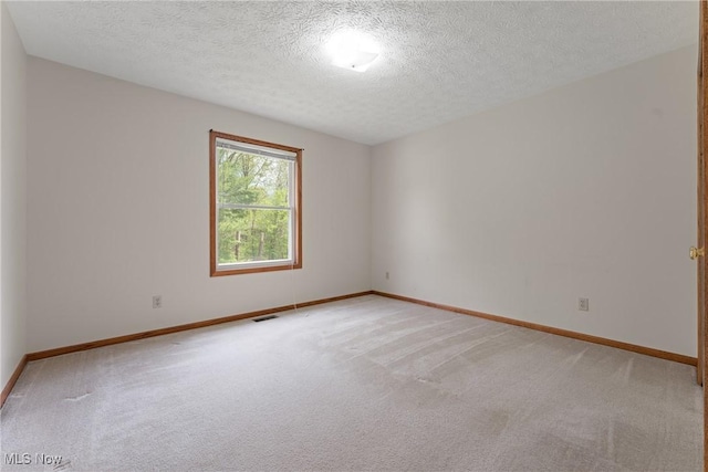 spare room featuring baseboards, a textured ceiling, visible vents, and light colored carpet