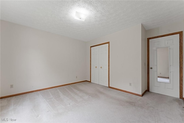 unfurnished bedroom with light colored carpet, a closet, a textured ceiling, and baseboards