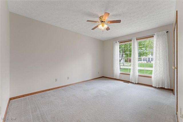 spare room with a textured ceiling, visible vents, baseboards, ceiling fan, and light carpet