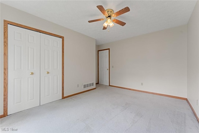 unfurnished bedroom featuring a ceiling fan, a closet, visible vents, baseboards, and light colored carpet