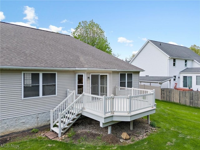 rear view of house with a yard, a deck, a shingled roof, and fence