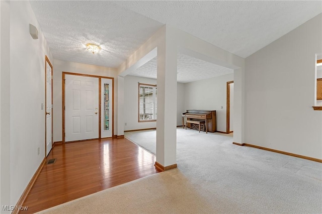 entryway with a textured ceiling, carpet floors, baseboards, and visible vents