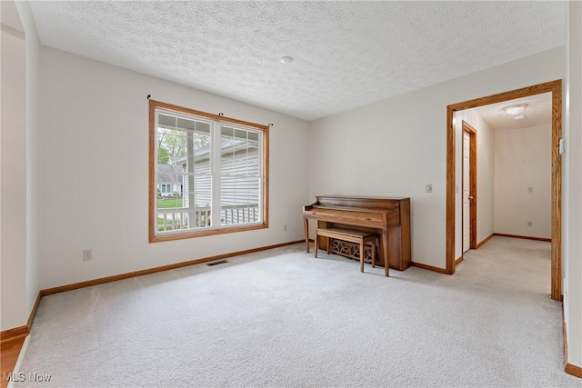 empty room featuring light colored carpet, a textured ceiling, visible vents, and baseboards