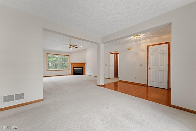 unfurnished living room with a textured ceiling, visible vents, carpet floors, baseboards, and a glass covered fireplace