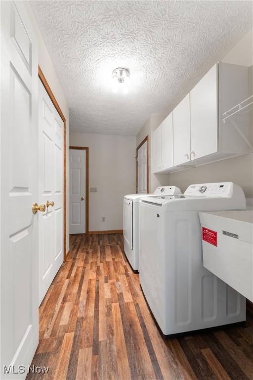 clothes washing area featuring cabinet space, a textured ceiling, light wood-type flooring, washing machine and dryer, and baseboards