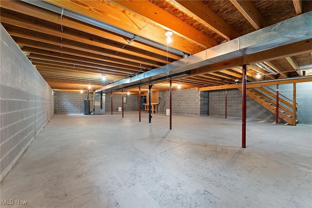 unfinished below grade area with gas water heater, stairs, heating unit, and concrete block wall