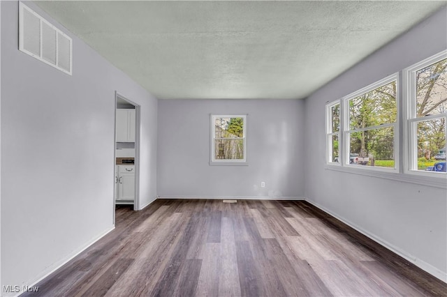 empty room featuring a wealth of natural light, dark wood finished floors, visible vents, and a textured ceiling