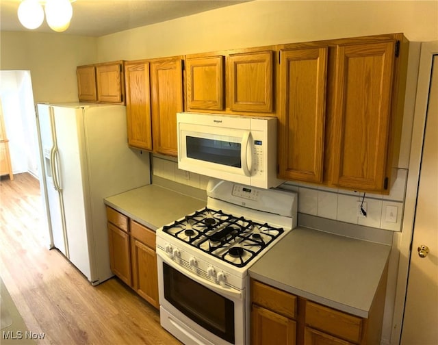 kitchen with brown cabinetry, white appliances, light wood-type flooring, and decorative backsplash