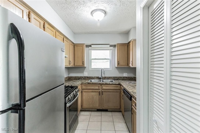 kitchen with a textured ceiling, light tile patterned flooring, a sink, dark countertops, and appliances with stainless steel finishes