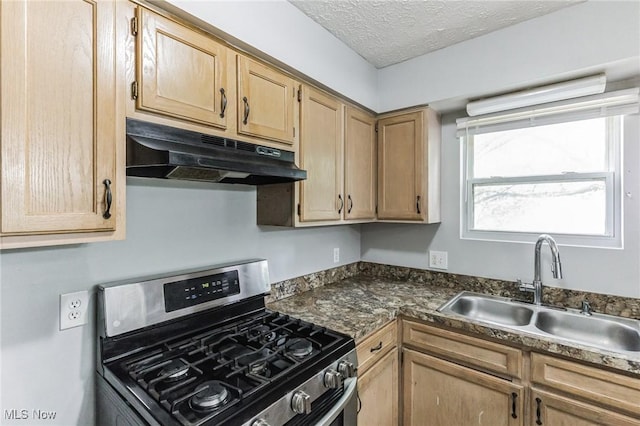 kitchen with light brown cabinetry, a textured ceiling, under cabinet range hood, stainless steel gas stove, and a sink