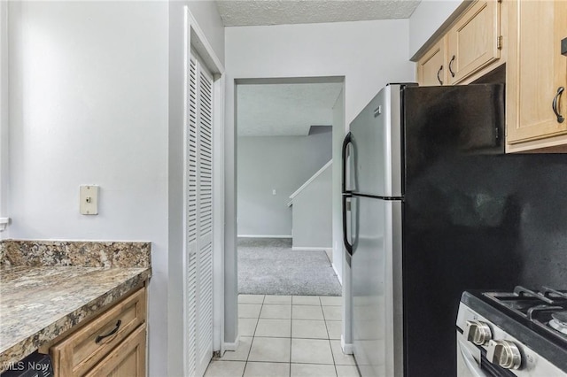 kitchen with light tile patterned floors, stainless steel appliances, baseboards, and light carpet