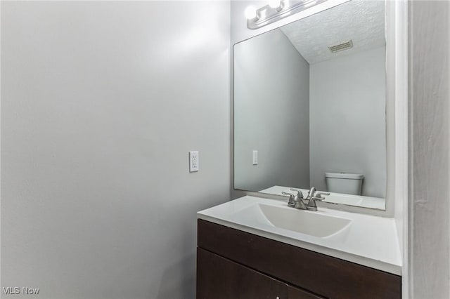 bathroom featuring a textured ceiling, visible vents, toilet, and vanity