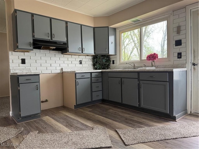 kitchen with under cabinet range hood, tasteful backsplash, dark wood-style floors, and gray cabinets