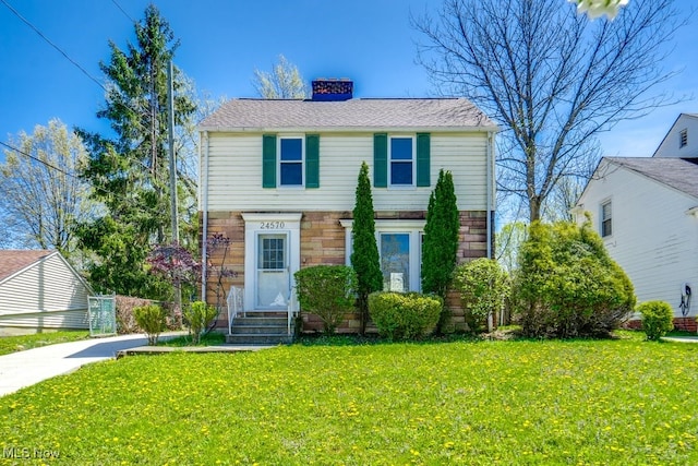 colonial inspired home featuring a front lawn, a chimney, and stone siding