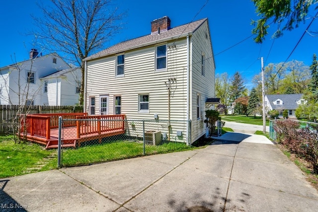 rear view of property with central AC, fence, a chimney, a deck, and a lawn