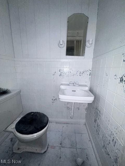half bath with a sink, toilet, tile walls, and a wainscoted wall