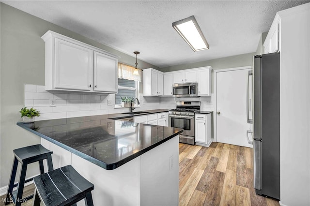 kitchen featuring appliances with stainless steel finishes, a peninsula, a sink, light wood-style flooring, and white cabinetry