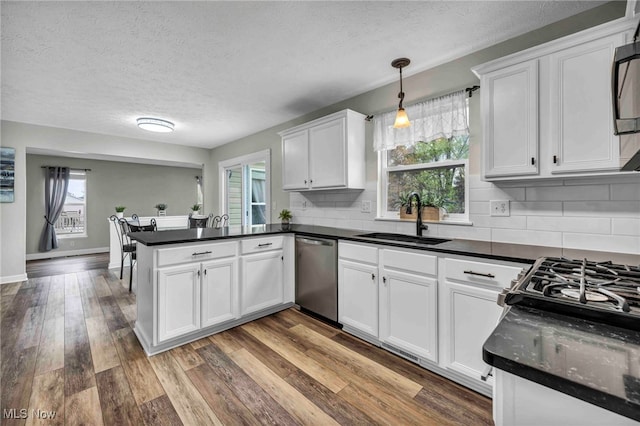 kitchen featuring stainless steel dishwasher, a peninsula, a textured ceiling, a sink, and white cabinets