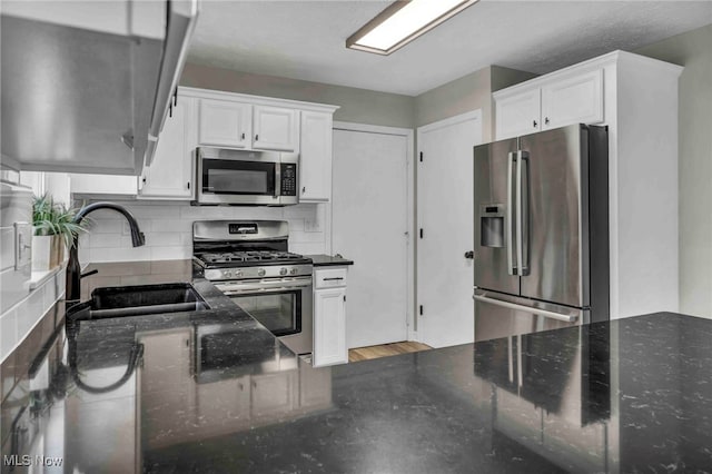 kitchen with stainless steel appliances, a sink, white cabinets, and backsplash