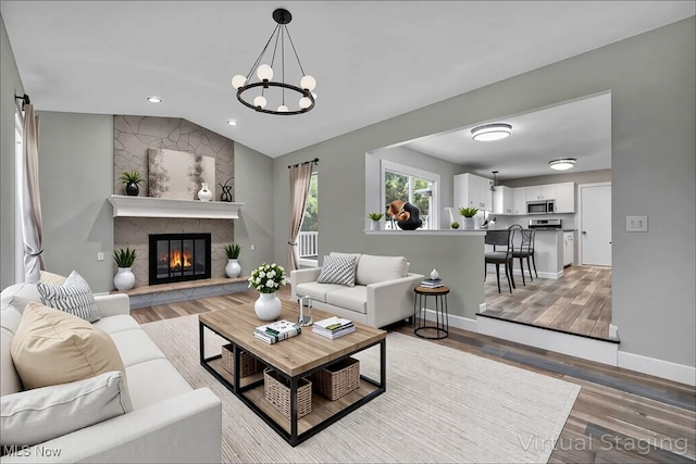 living room featuring lofted ceiling, wood finished floors, a fireplace, an inviting chandelier, and baseboards