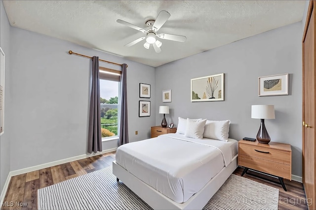 bedroom featuring dark wood-style floors, baseboards, ceiling fan, and a textured ceiling