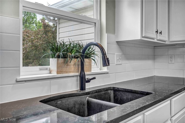 room details with white cabinetry, tasteful backsplash, dark stone countertops, and a sink