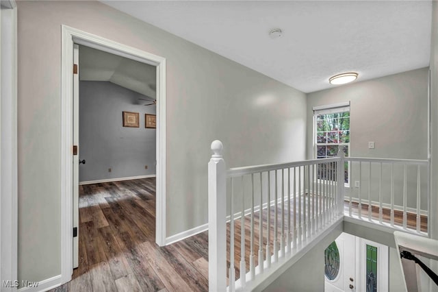hallway with wood finished floors, baseboards, an upstairs landing, and lofted ceiling