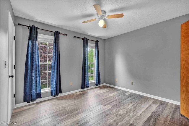unfurnished room with a ceiling fan, baseboards, a textured ceiling, and wood finished floors