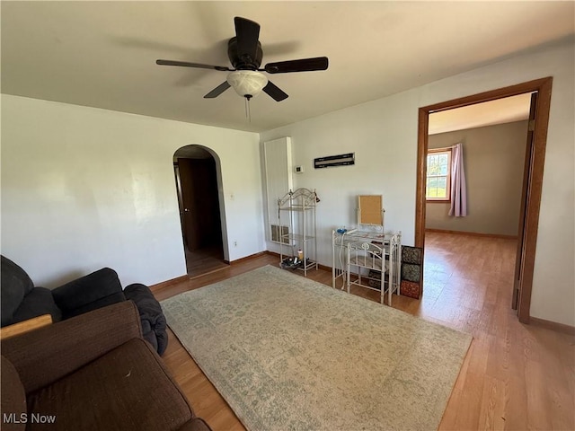 living area with arched walkways, baseboards, a ceiling fan, and wood finished floors
