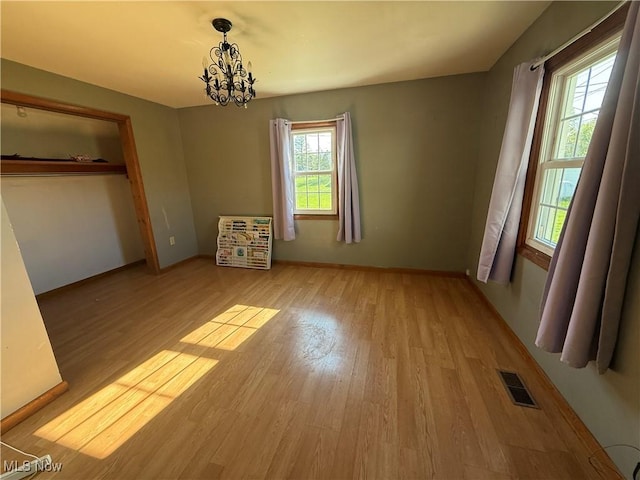 unfurnished bedroom with baseboards, a notable chandelier, light wood-type flooring, and visible vents