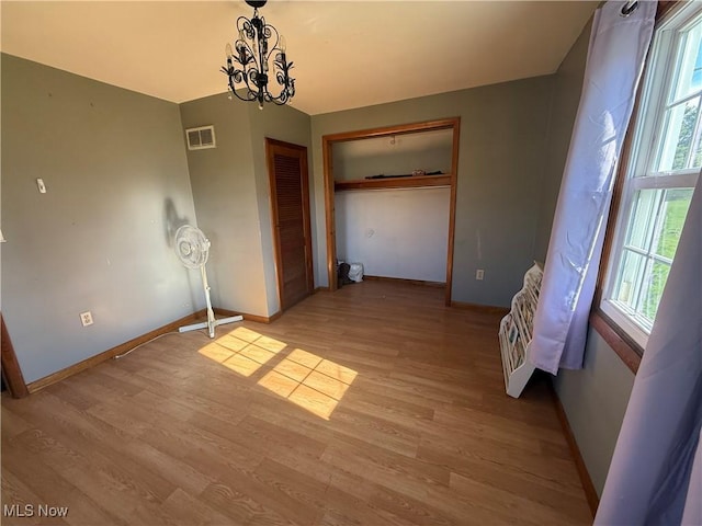 unfurnished bedroom with light wood-style floors, visible vents, baseboards, and a notable chandelier