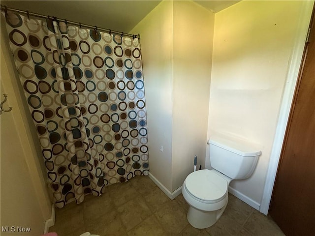 bathroom featuring toilet, a shower with shower curtain, and baseboards
