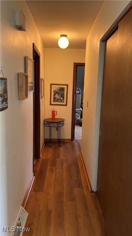 corridor with baseboards, visible vents, and wood finished floors