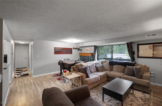 living area featuring a textured ceiling, light wood-style flooring, and baseboards