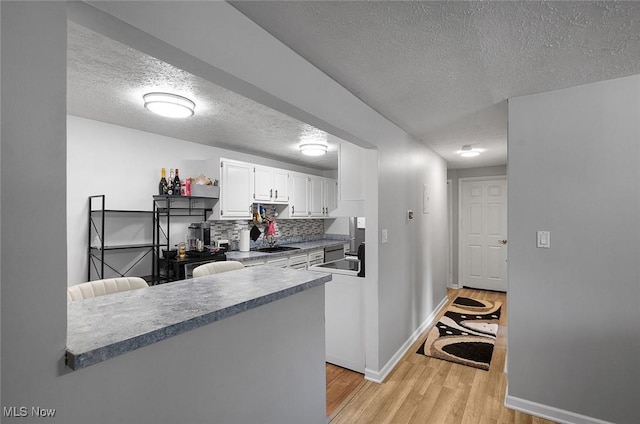 kitchen with a textured ceiling, light wood-style floors, baseboards, white cabinets, and a sink