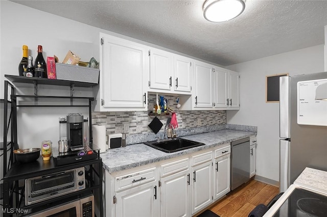 kitchen featuring a sink, appliances with stainless steel finishes, light countertops, light wood-style flooring, and white cabinets