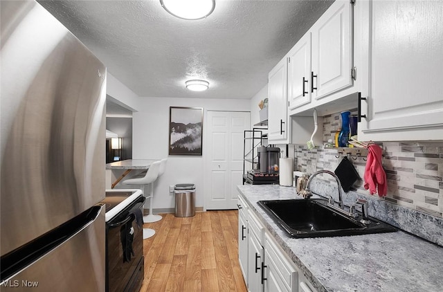 kitchen featuring freestanding refrigerator, electric range, a sink, decorative backsplash, and light wood finished floors