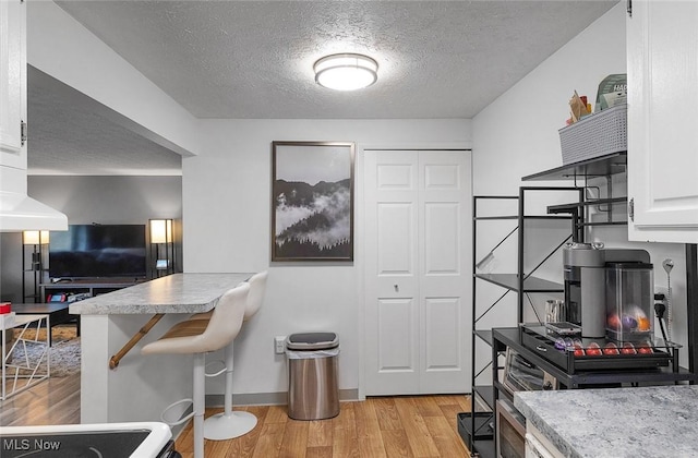 kitchen featuring light wood-style floors, white cabinets, a textured ceiling, light countertops, and baseboards
