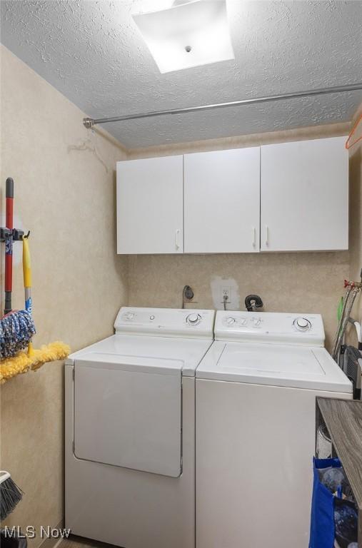 clothes washing area with cabinet space, separate washer and dryer, and a textured ceiling