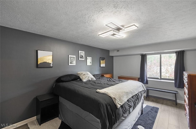 bedroom with a textured ceiling, wood finished floors, and baseboards