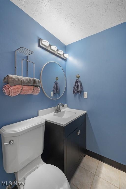 bathroom with a textured ceiling, toilet, tile patterned flooring, and vanity