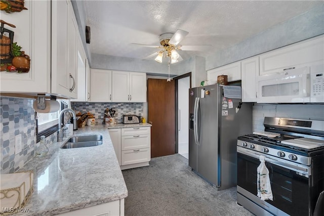 kitchen with stainless steel appliances, a sink, ceiling fan, decorative backsplash, and white cabinetry