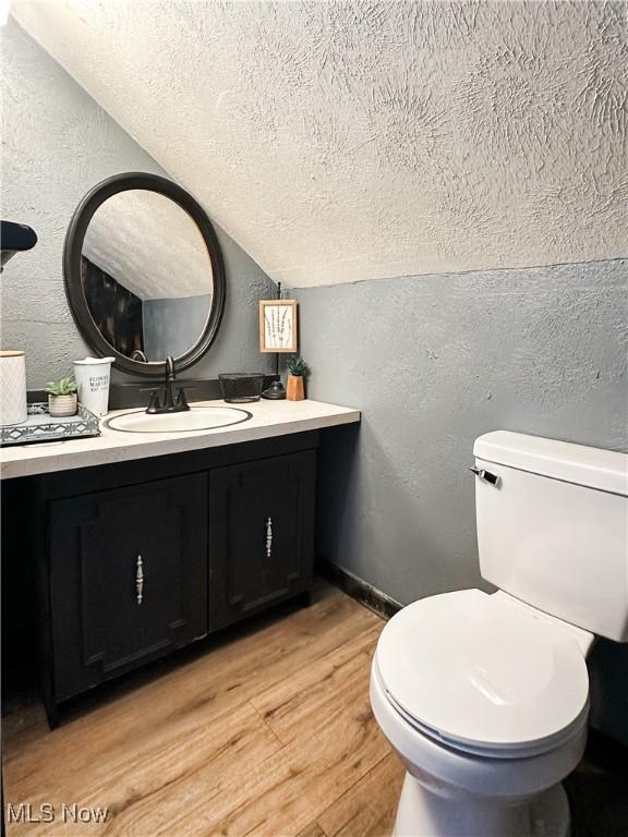 bathroom with a textured wall, vaulted ceiling, wood finished floors, a textured ceiling, and toilet